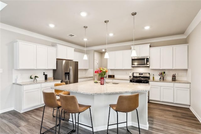 kitchen with white cabinets, appliances with stainless steel finishes, pendant lighting, and an island with sink