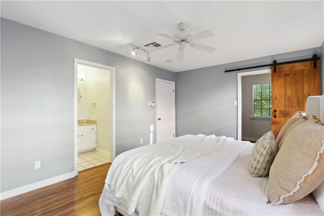 bedroom featuring a barn door, ensuite bathroom, ceiling fan, and dark hardwood / wood-style floors