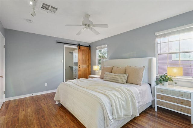 bedroom featuring a barn door, dark hardwood / wood-style floors, and ceiling fan