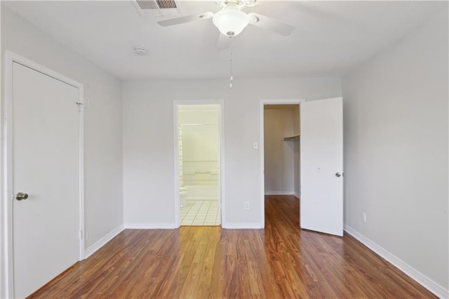 unfurnished bedroom with dark wood-type flooring, ensuite bathroom, ceiling fan, a spacious closet, and a closet