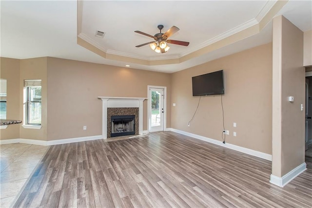 unfurnished living room featuring a raised ceiling, ceiling fan, crown molding, and light wood-type flooring