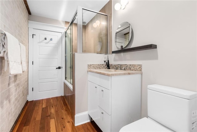 bathroom featuring wood-type flooring, brick wall, walk in shower, and toilet