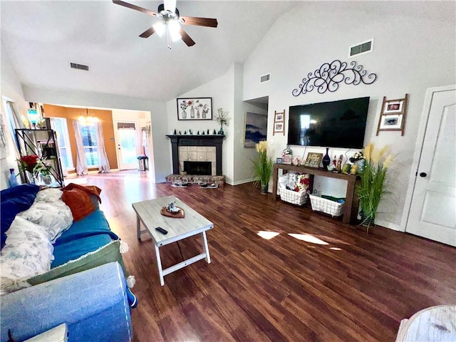 living room featuring vaulted ceiling, a tiled fireplace, ceiling fan with notable chandelier, and dark hardwood / wood-style floors