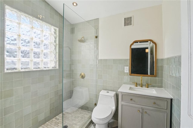 bathroom with tiled shower, toilet, tile walls, and vanity