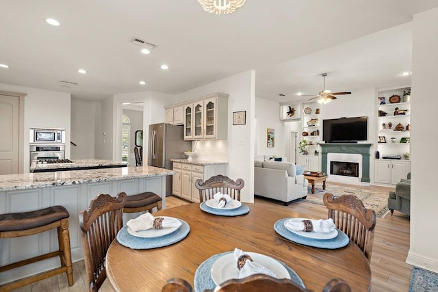 dining room with built in shelves, ceiling fan, and light hardwood / wood-style flooring