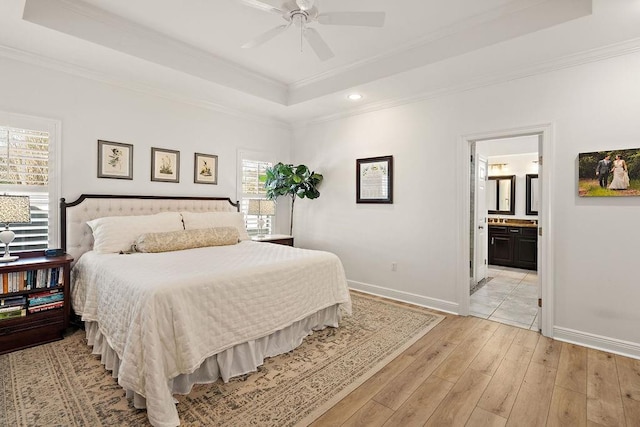 bedroom with ensuite bath, ceiling fan, ornamental molding, a tray ceiling, and light hardwood / wood-style floors