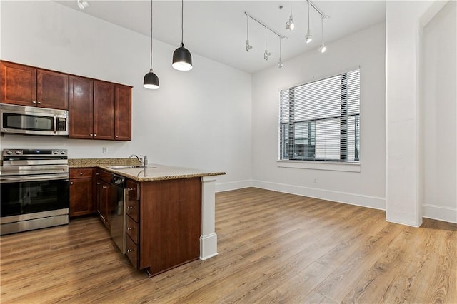 kitchen with kitchen peninsula, light stone countertops, stainless steel appliances, decorative light fixtures, and light hardwood / wood-style flooring