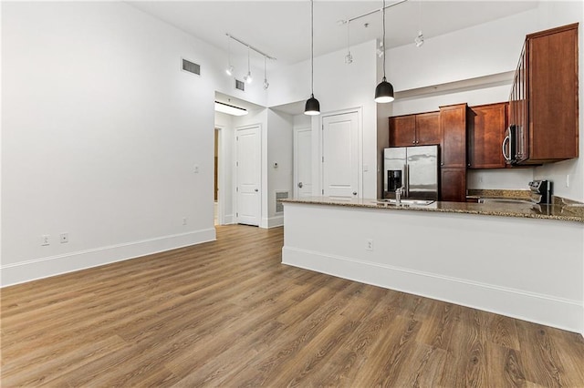 kitchen with light stone countertops, appliances with stainless steel finishes, wood-type flooring, pendant lighting, and a high ceiling