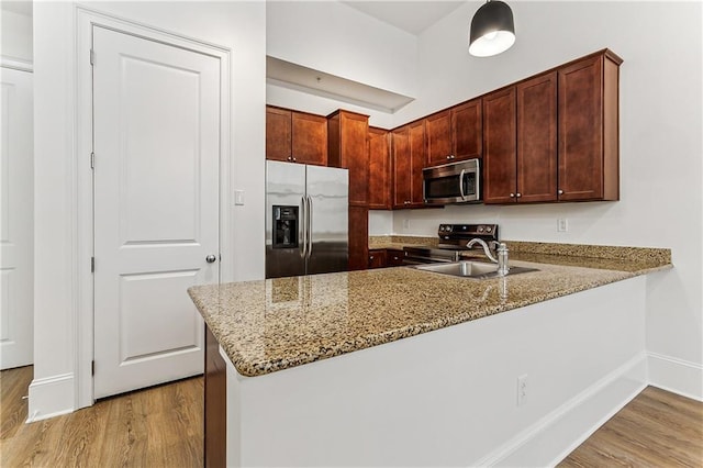 kitchen featuring kitchen peninsula, light stone countertops, light wood-type flooring, stainless steel appliances, and sink