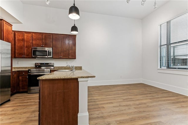 kitchen featuring pendant lighting, sink, light stone countertops, appliances with stainless steel finishes, and kitchen peninsula