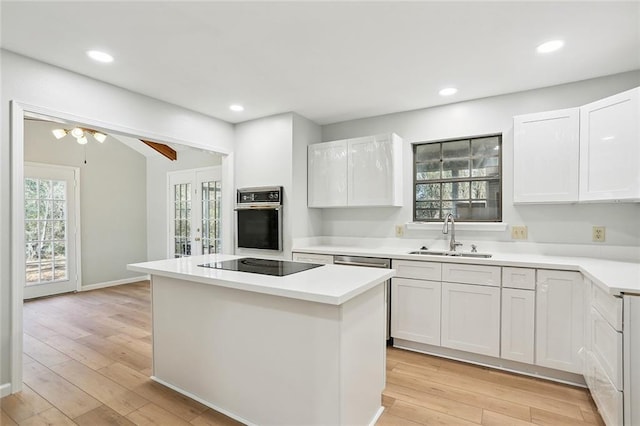 kitchen with a center island, stainless steel oven, black electric stovetop, white cabinets, and sink