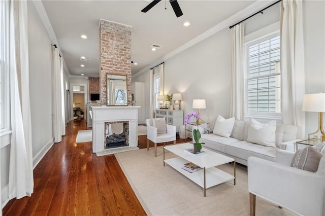 living room featuring a brick fireplace, hardwood / wood-style floors, ceiling fan, and crown molding