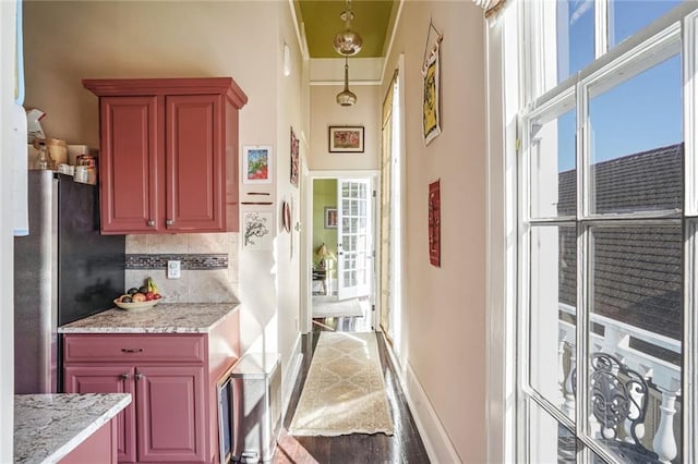 interior space with light stone countertops, decorative light fixtures, tasteful backsplash, and stainless steel refrigerator