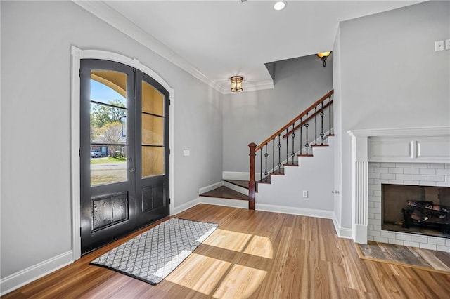 entryway featuring ornamental molding, wood-type flooring, a fireplace, and french doors