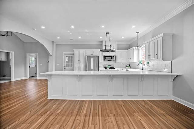 kitchen with white cabinets, hanging light fixtures, appliances with stainless steel finishes, tasteful backsplash, and kitchen peninsula