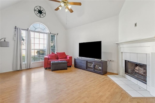 living room with ceiling fan, light hardwood / wood-style floors, high vaulted ceiling, and a tiled fireplace