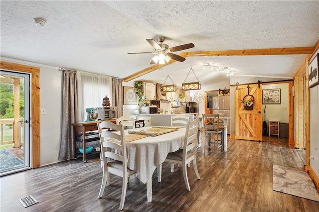 dining space with a textured ceiling, ceiling fan, a barn door, lofted ceiling with beams, and dark hardwood / wood-style floors