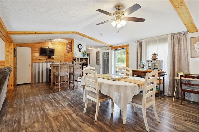 dining room featuring wooden walls, vaulted ceiling with beams, ceiling fan, a textured ceiling, and dark hardwood / wood-style flooring