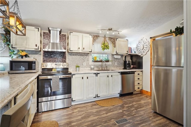 kitchen with appliances with stainless steel finishes, wall chimney exhaust hood, sink, white cabinets, and dark hardwood / wood-style floors