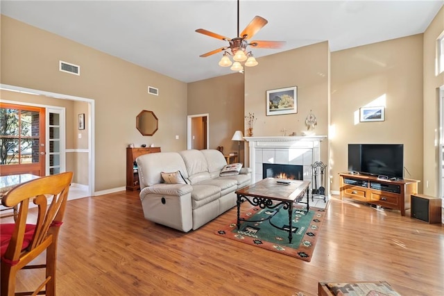 living room with light hardwood / wood-style flooring, ceiling fan, and a tiled fireplace