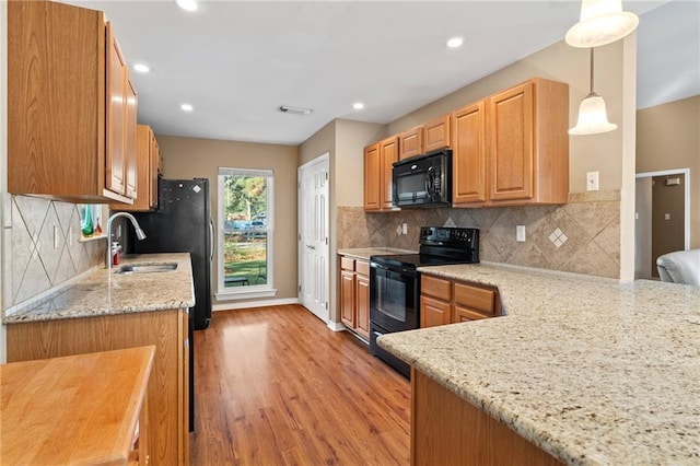 kitchen featuring decorative backsplash, kitchen peninsula, light stone countertops, black appliances, and pendant lighting