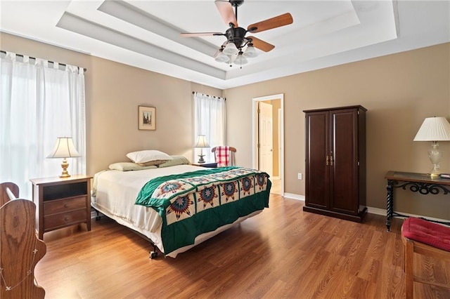 bedroom featuring a raised ceiling, ceiling fan, and light wood-type flooring