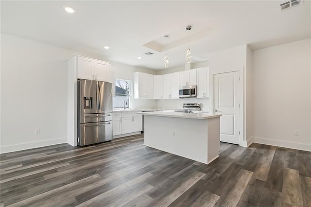 kitchen featuring appliances with stainless steel finishes, hanging light fixtures, dark wood-type flooring, white cabinets, and a kitchen island