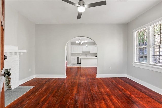 unfurnished living room with dark hardwood / wood-style floors, ceiling fan with notable chandelier, and a brick fireplace