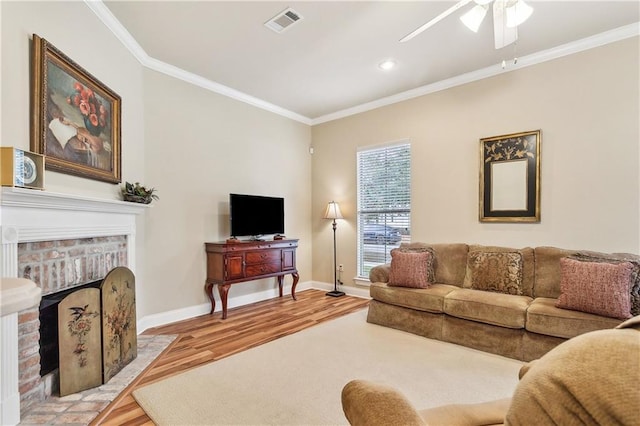 living room with a brick fireplace, ceiling fan, crown molding, and light hardwood / wood-style flooring