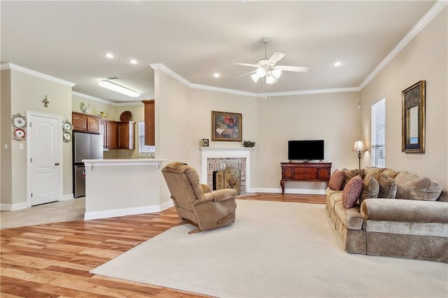 living room with a brick fireplace, ceiling fan, crown molding, and light hardwood / wood-style flooring