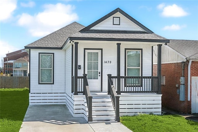 bungalow featuring covered porch, a shingled roof, a front yard, and fence