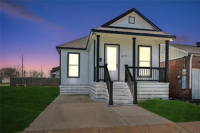 view of front facade with covered porch, a shingled roof, and a front yard