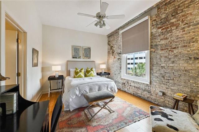 bedroom with ceiling fan, hardwood / wood-style floors, and brick wall