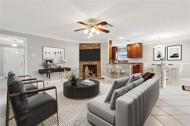 tiled living room featuring ceiling fan, sink, crown molding, and a fireplace