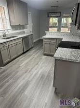 kitchen with light stone counters, kitchen peninsula, light wood-type flooring, and sink