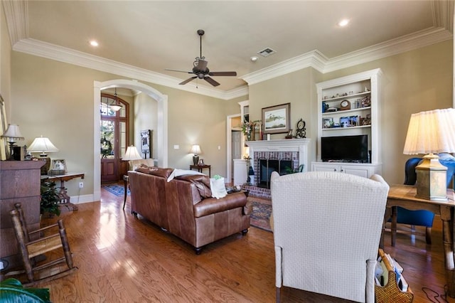 living room featuring a fireplace, built in features, crown molding, and hardwood / wood-style floors