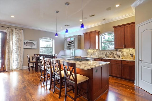 kitchen featuring light stone counters, decorative light fixtures, a kitchen bar, a kitchen island, and ornamental molding