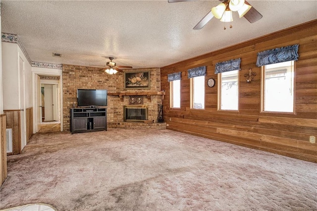 unfurnished living room with a textured ceiling, a brick fireplace, wooden walls, and carpet