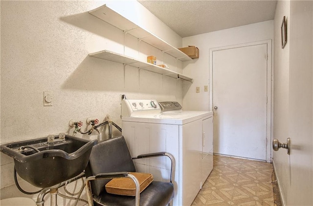 clothes washing area with sink, a textured ceiling, and washing machine and clothes dryer