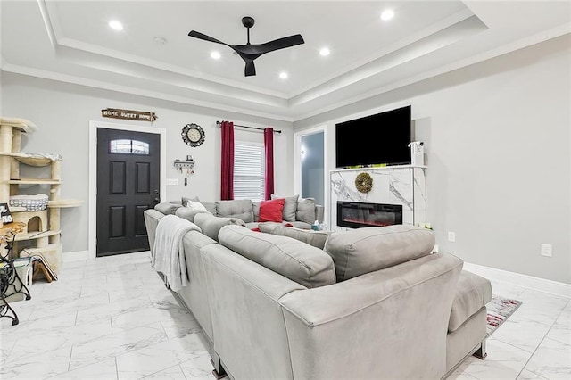 living room with ceiling fan, crown molding, a fireplace, and a tray ceiling