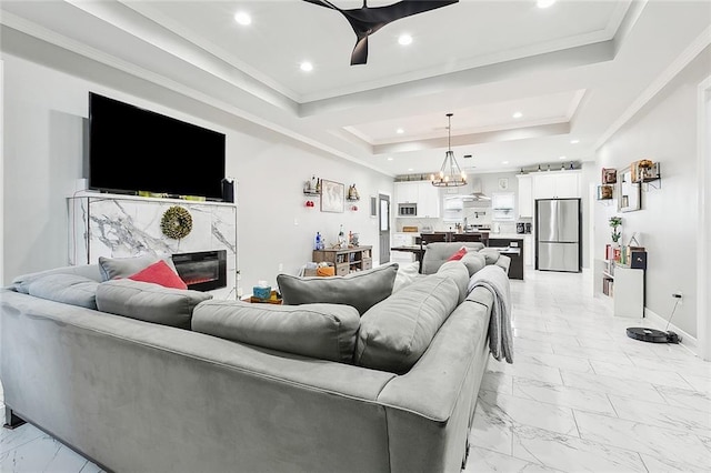 living room featuring a premium fireplace, a raised ceiling, and a chandelier