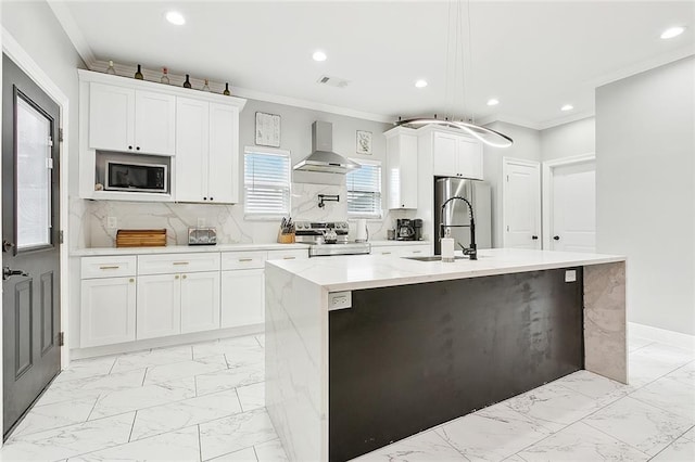 kitchen with wall chimney range hood, decorative backsplash, a kitchen island with sink, white cabinets, and appliances with stainless steel finishes