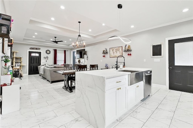 kitchen with a kitchen island with sink, a raised ceiling, ceiling fan, light stone counters, and white cabinets