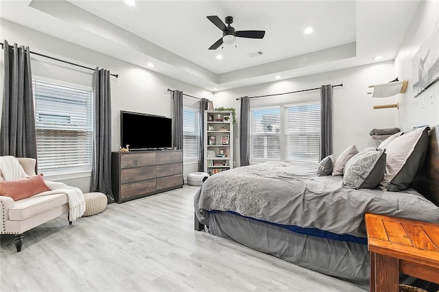 bedroom with ceiling fan, a tray ceiling, and light hardwood / wood-style flooring