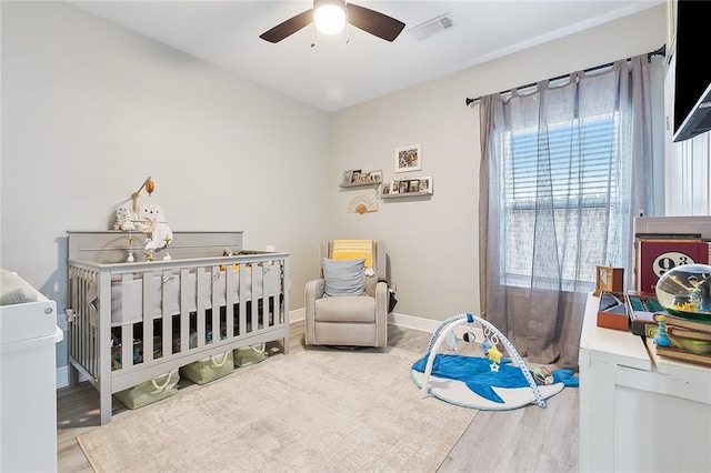 bedroom with ceiling fan, a crib, and hardwood / wood-style floors