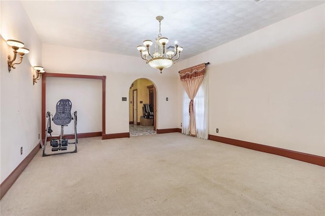 spare room featuring light carpet and a notable chandelier