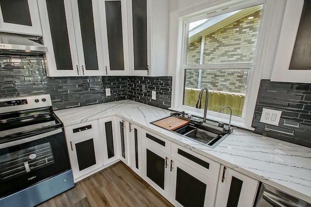 kitchen featuring stainless steel electric range, a healthy amount of sunlight, light stone counters, sink, and white cabinetry