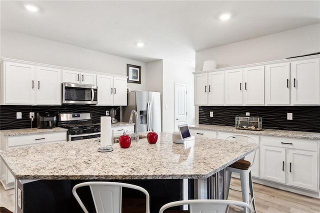 kitchen featuring a breakfast bar area, stainless steel appliances, an island with sink, white cabinets, and tasteful backsplash