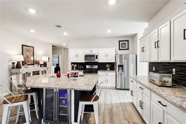 kitchen with stainless steel appliances, white cabinets, light stone countertops, a center island with sink, and a breakfast bar