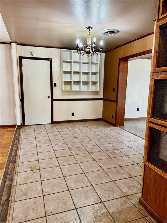 unfurnished dining area featuring ornamental molding, a notable chandelier, and light tile patterned floors